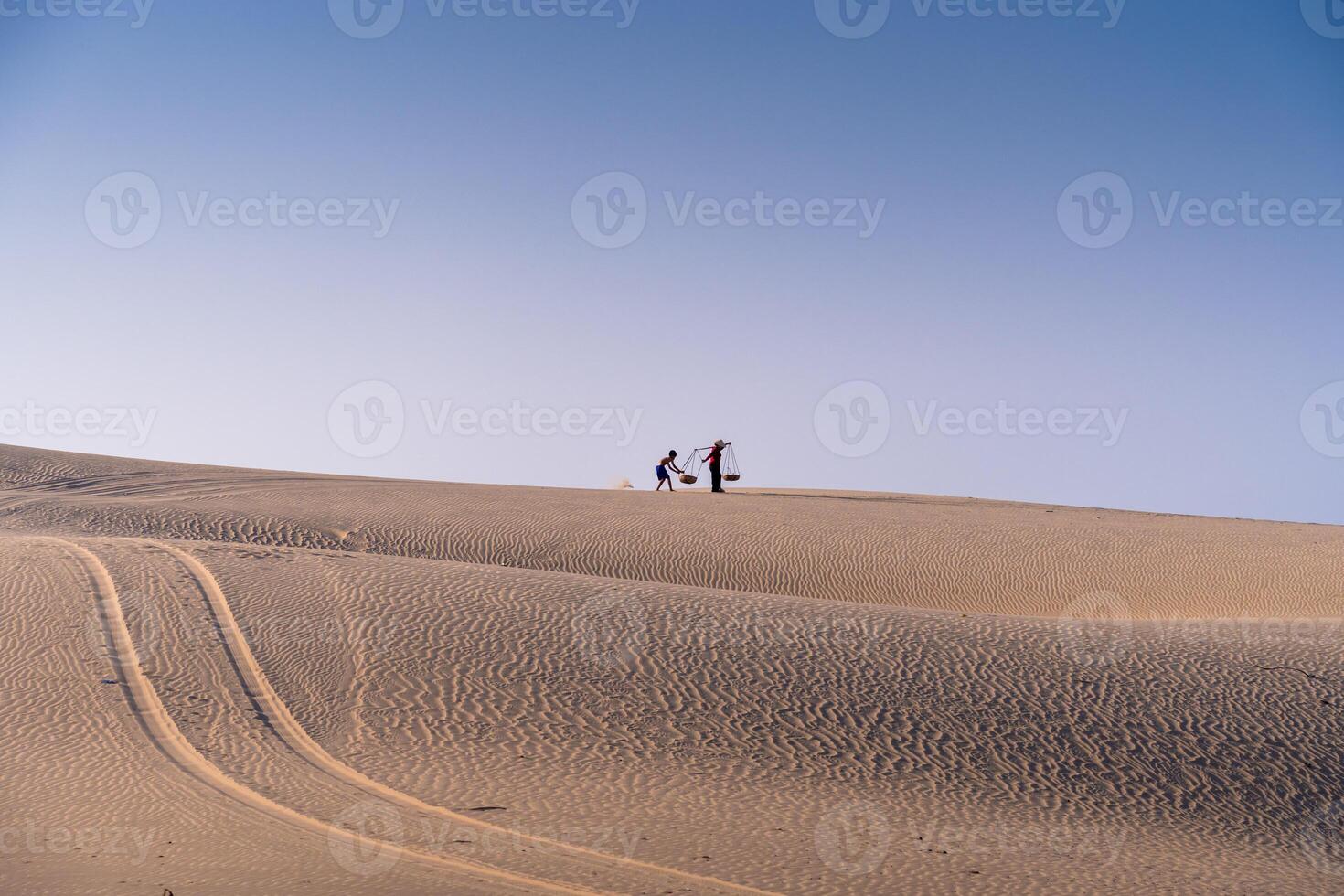 Aerial view of a peasant woman carries a bamboo frame on the shoulder across sand dunes in Ninh Thuan province, Vietnam. It is one of the most beautiful places in Vietnam photo