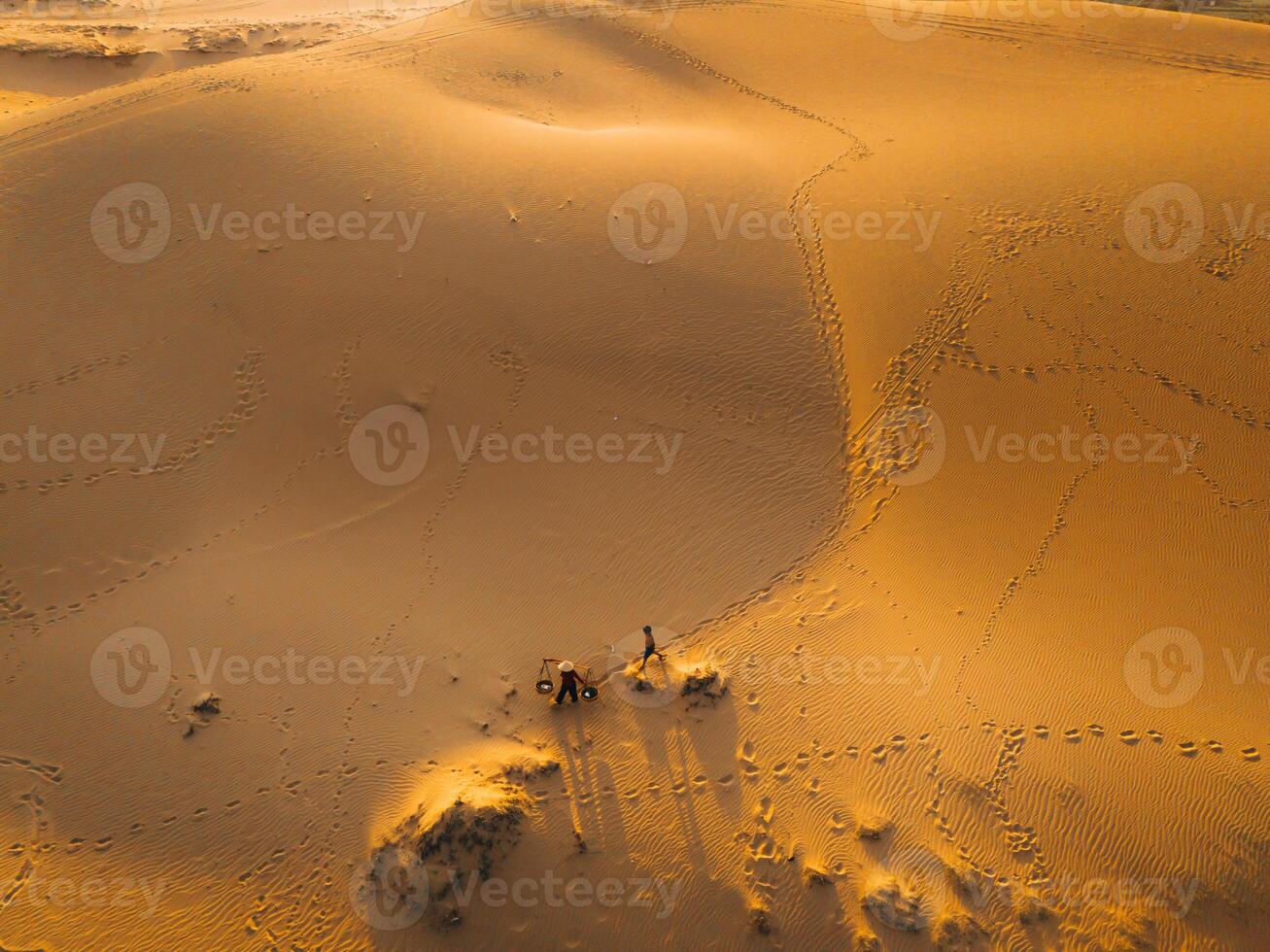 Aerial view of a peasant woman carries a bamboo frame on the shoulder across sand dunes in Ninh Thuan province, Vietnam. It is one of the most beautiful places in Vietnam photo