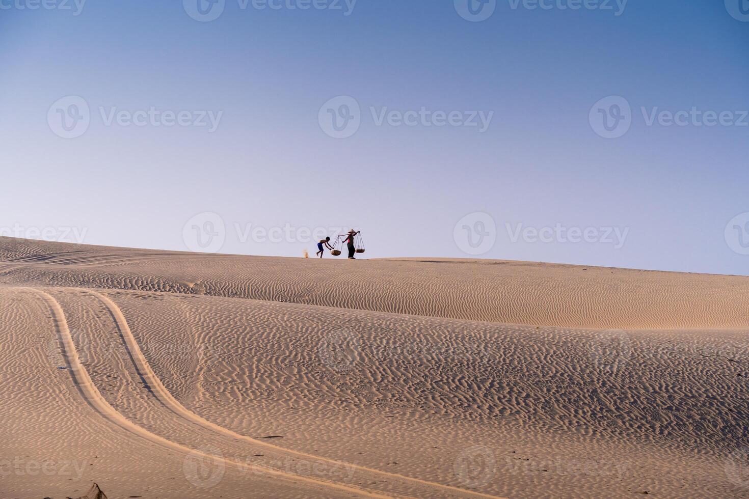 Aerial view of a peasant woman carries a bamboo frame on the shoulder across sand dunes in Ninh Thuan province, Vietnam. It is one of the most beautiful places in Vietnam photo