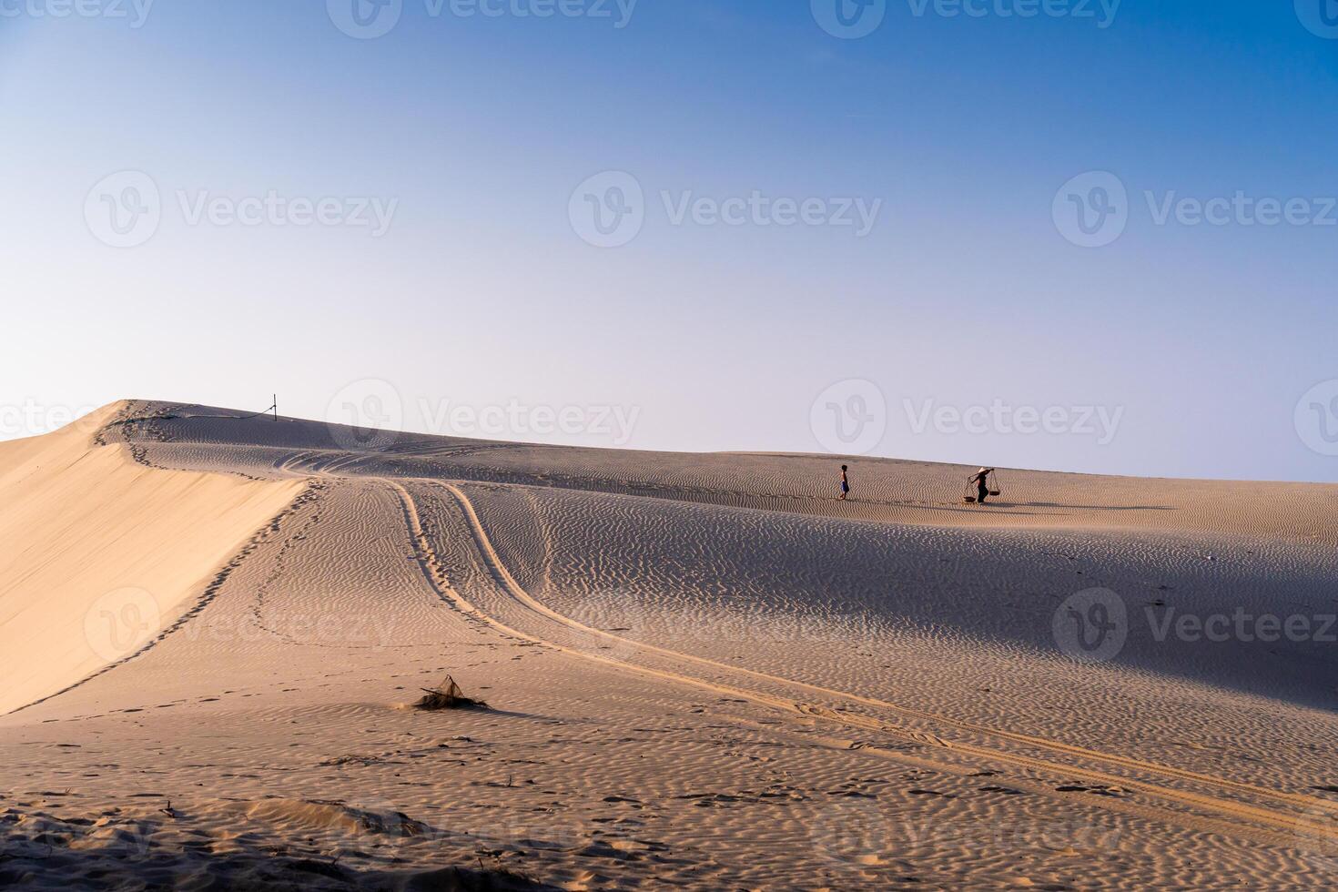 Aerial view of a peasant woman carries a bamboo frame on the shoulder across sand dunes in Ninh Thuan province, Vietnam. It is one of the most beautiful places in Vietnam photo