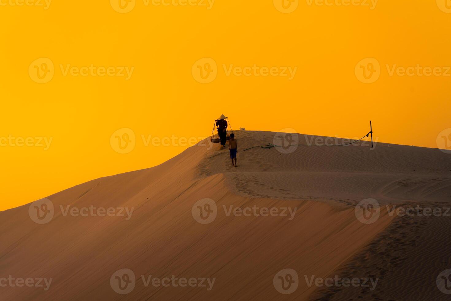 Aerial view of a peasant woman carries a bamboo frame on the shoulder across sand dunes in Ninh Thuan province, Vietnam. It is one of the most beautiful places in Vietnam photo