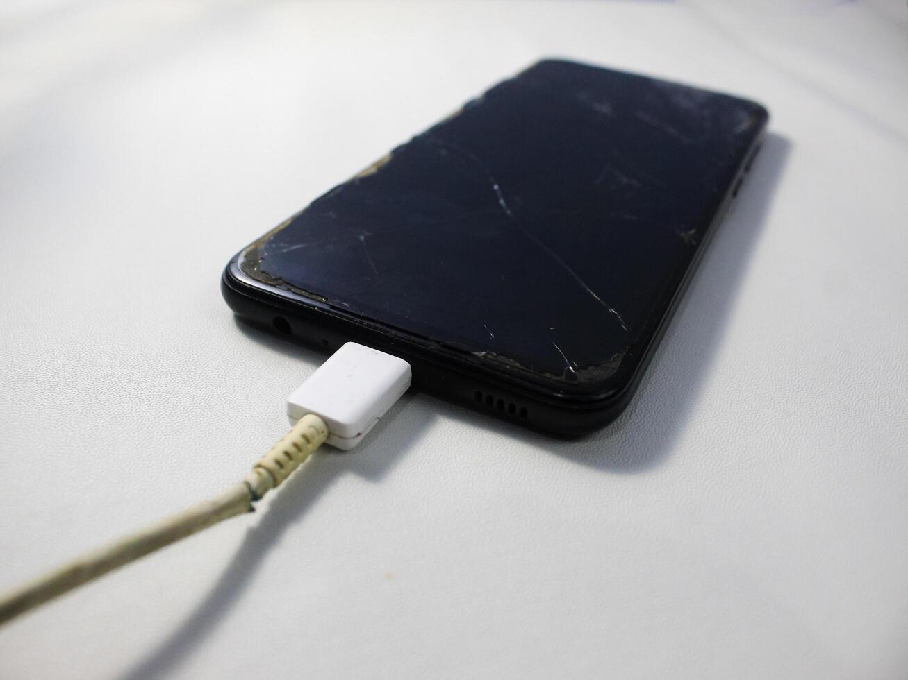 Old charger cable broken and smartphone, Defective charging cord, Connection deterioration device photo