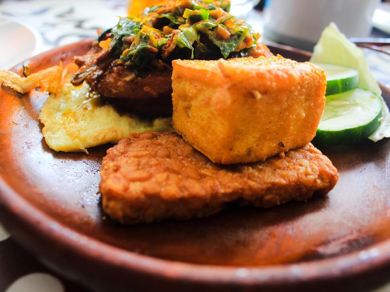 indonesio alimento. pollo penyet con chile salsa con tofu, tempeh, pepino, huevo y otro Fresco vegetales en madera plato foto