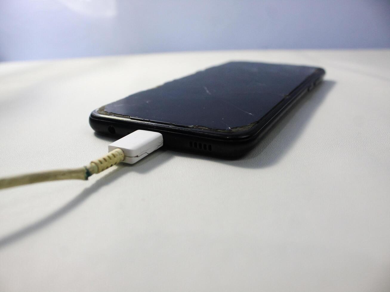 Old charger cable broken and smartphone, Defective charging cord, Connection deterioration device photo