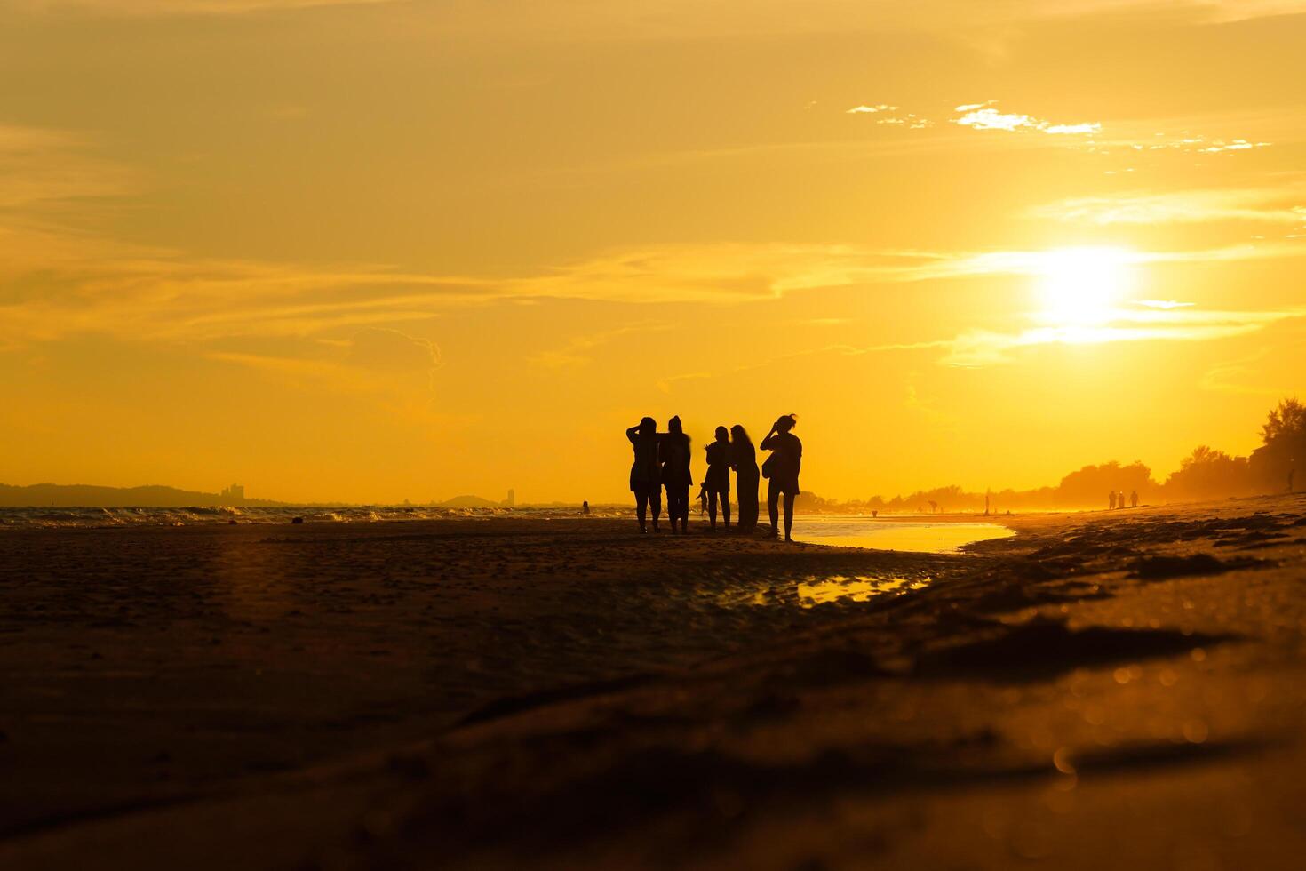 Silhouette of a group of friends enjoying the sunset on the beach at golden sunset time, relaxing on a relaxing vacation, sea in the evening. photo