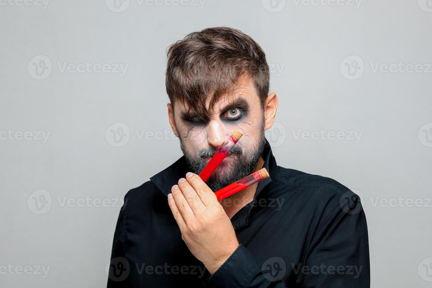 a bearded man with undead makeup for Halloween holds test tubes in which red liquid photo