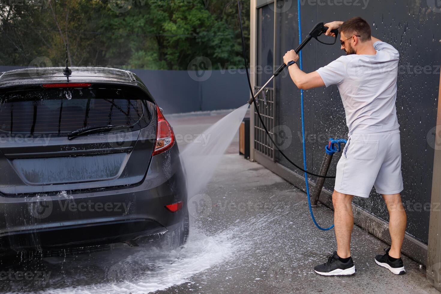 The car's at a car wash run by a man with a water cannon. A car at a self service car wash. photo