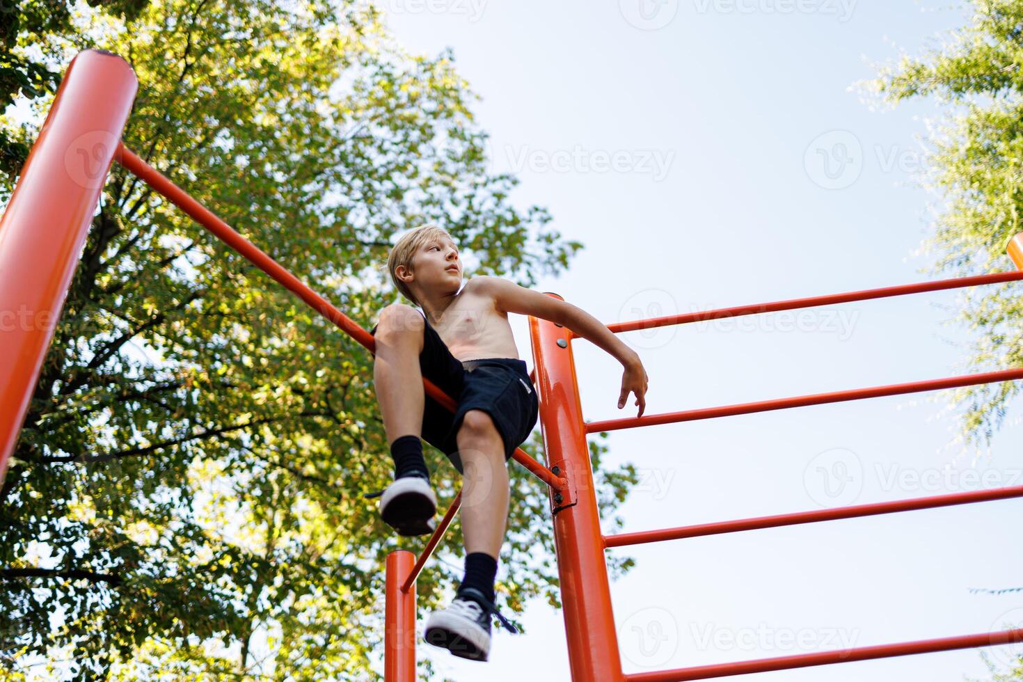 un adolescente chico subido arriba el gimnástico travesaño se sienta y descansa calle rutina de ejercicio en un horizontal bar en el colegio parque. foto