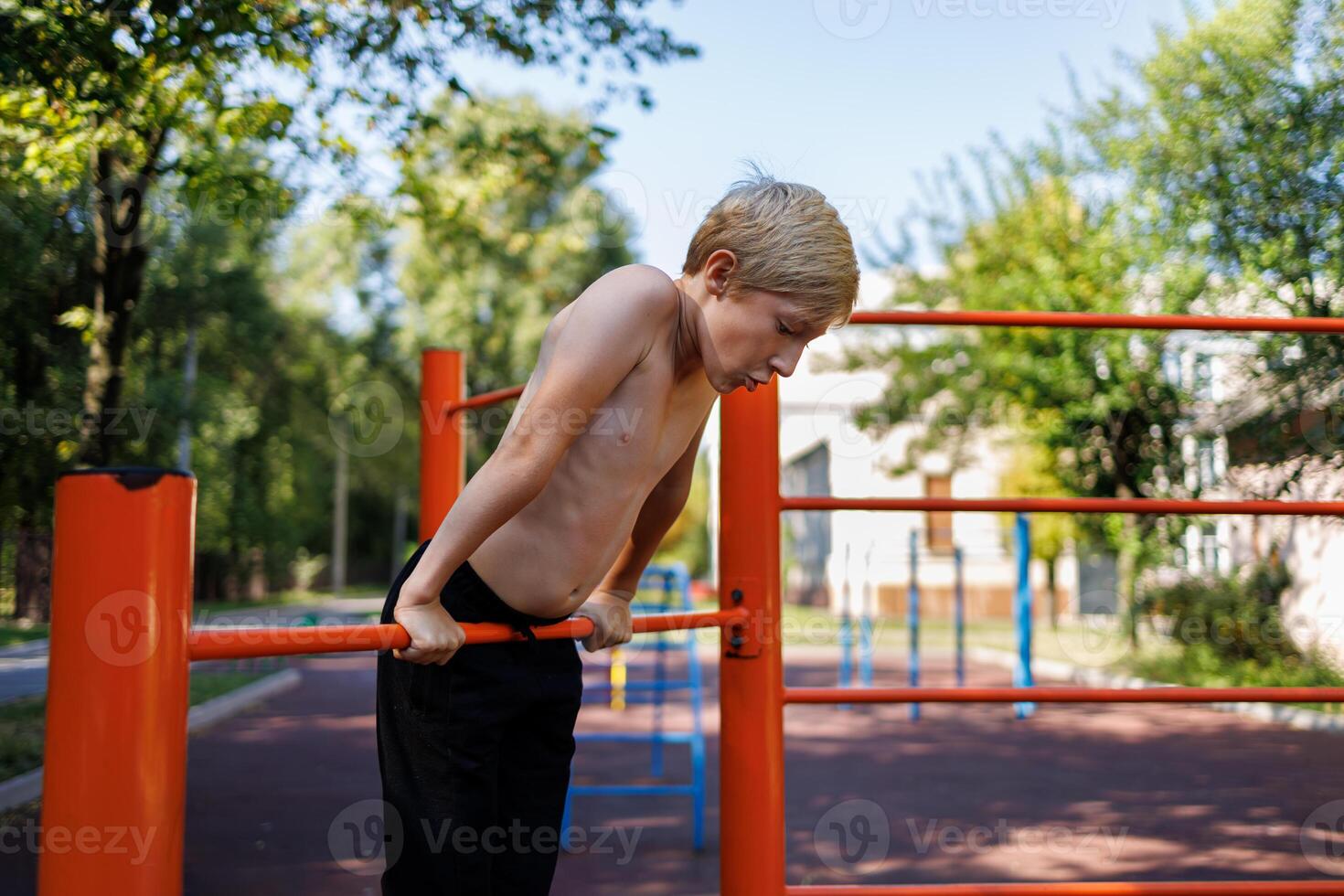 Sporty boy stretches up and holds on to the bar with his hands. Street workout on a horizontal bar in the school park. photo