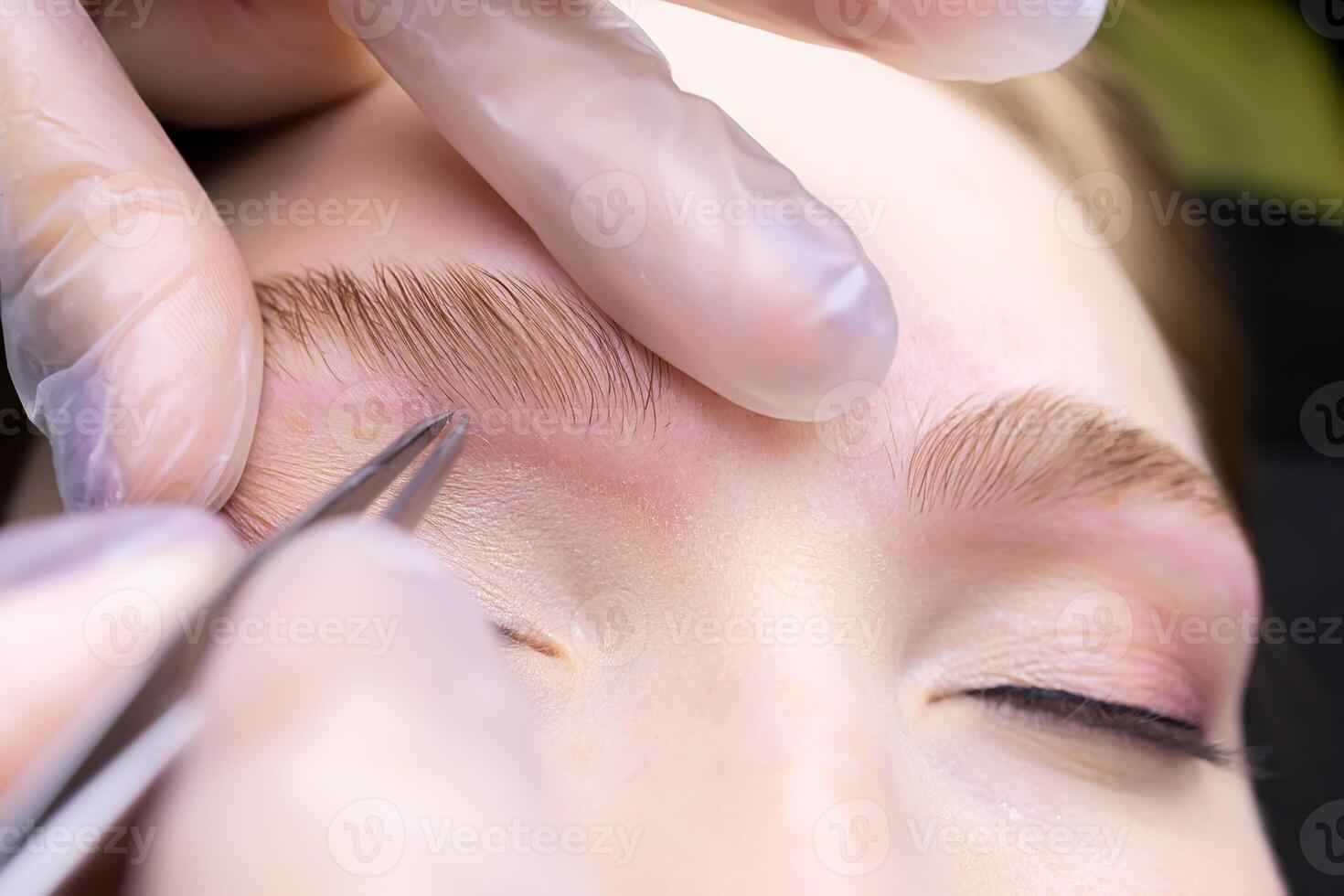 macro photography of the laid eyebrows with the help of lamination, the master tweezers pluck the contour of the eyebrows from excess hairs photo