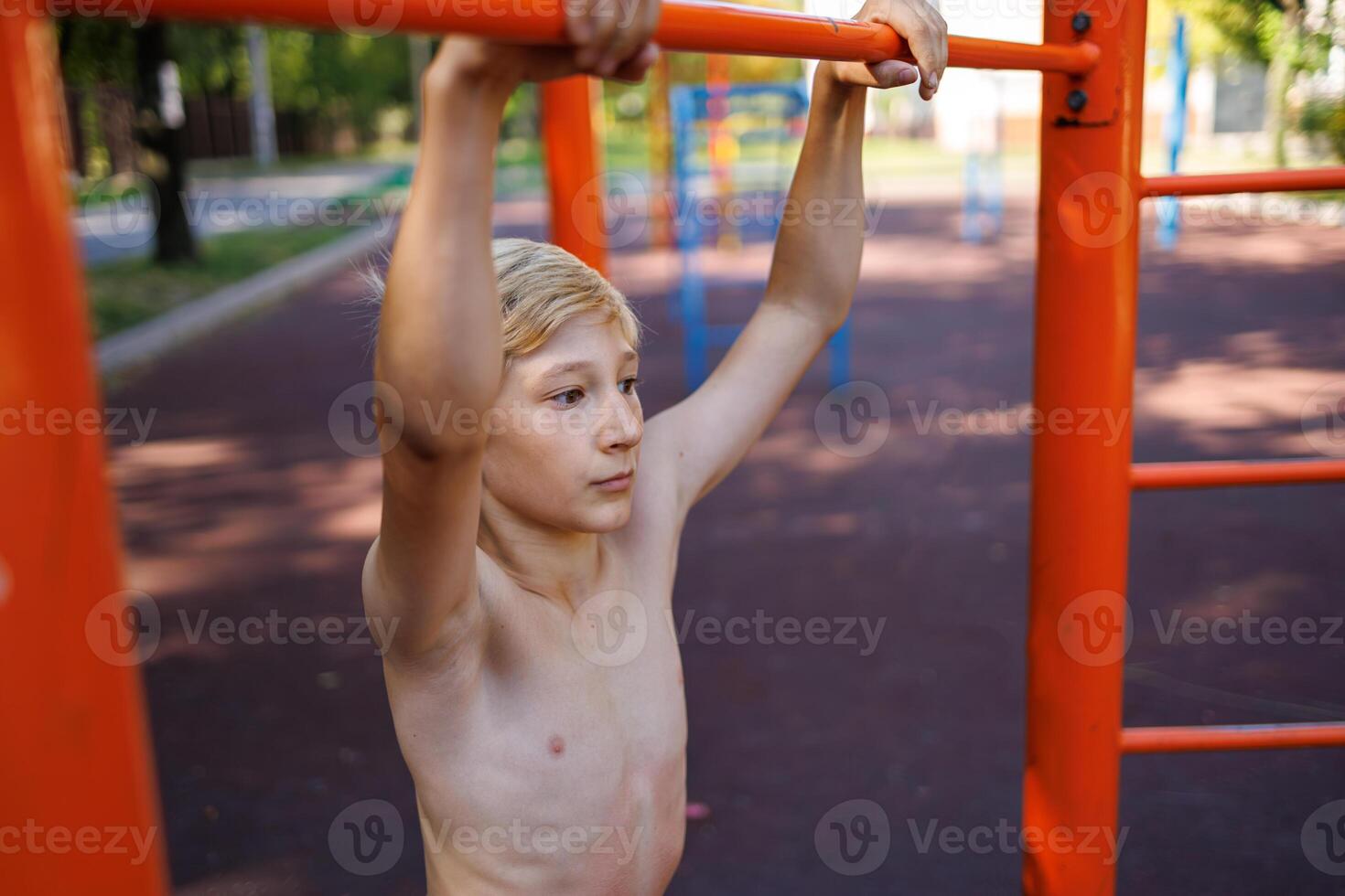 A teenager with an athletic development of musculature holds on to the horizontal bar. Street workout on a horizontal bar in the school park. photo