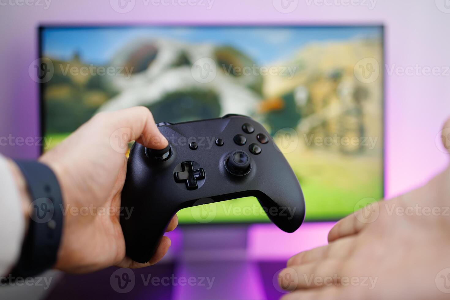 Holding a game gamepad in one hand and using the other hand to point at the monitor that's in the background. game gamepad in hand photo