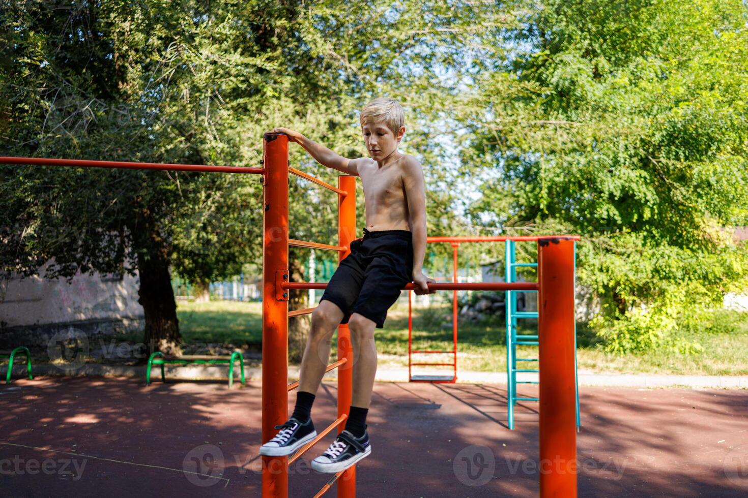 The teenager goes in for sports. Street workout on a horizontal bar in the school park. photo