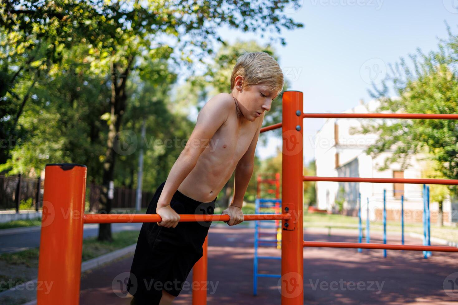 The athletic boy stretched himself up and holds on to the horizontal bar with his hands. Street workout on a horizontal bar in the school park. photo