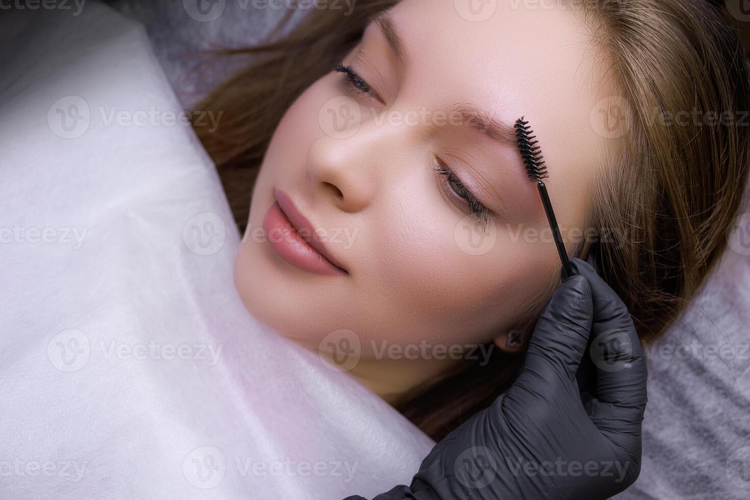 Eyebrow shape correction before the permanent makeup procedure using tweezers and a brush. PMU Procedure, Permanent Eyebrow Makeup. photo