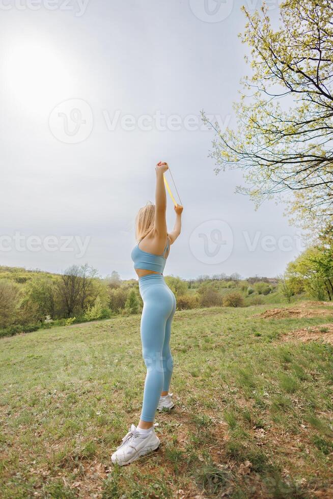Beautiful athletic girl doing exercises in the park. Beautiful blonde Caucasian woman in blue tight tracksuit. Blonde girl at an outdoor training session photo