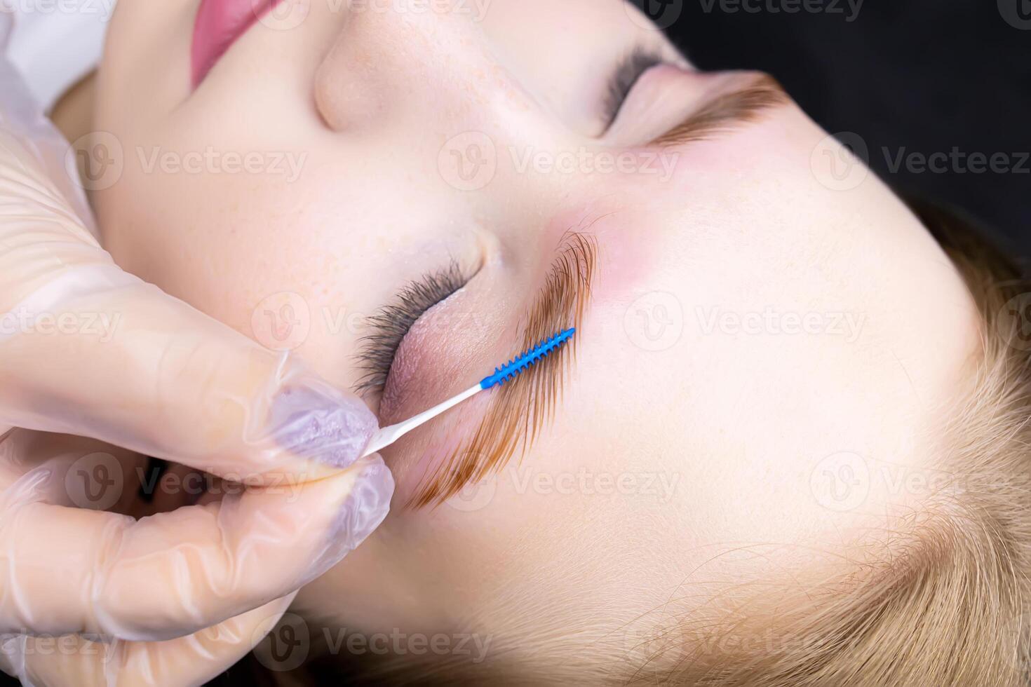 model during the eyebrow lamination procedure, the master combs the eyebrows with a special brush photo