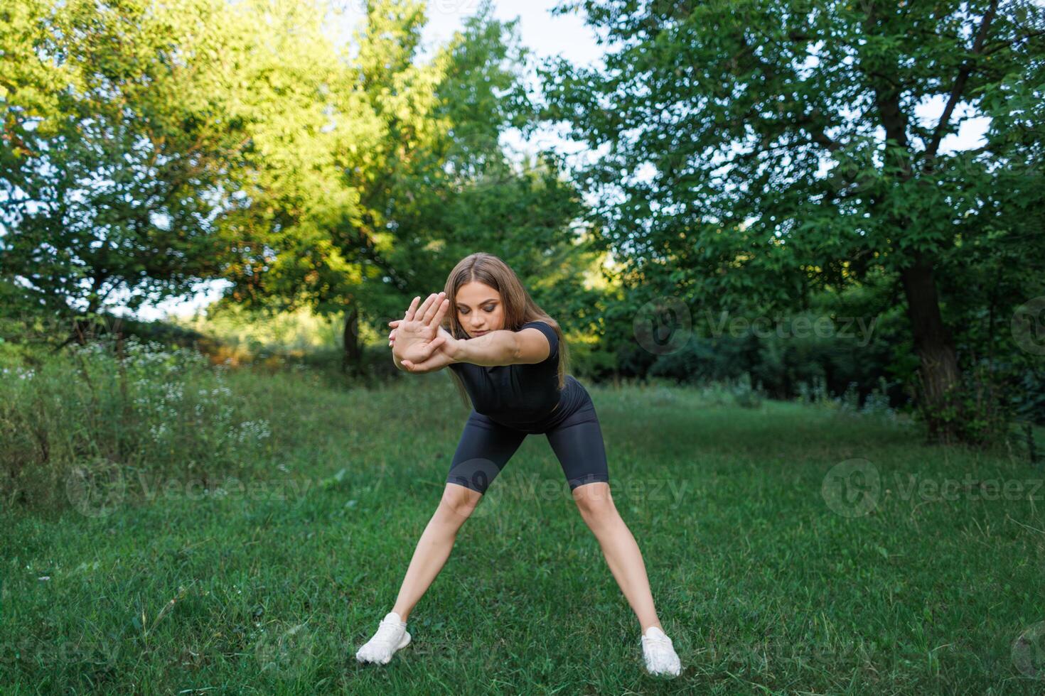 A young girl doing exercises in the park. Athletic girl in a tight uniform working outdoors in the park. photo