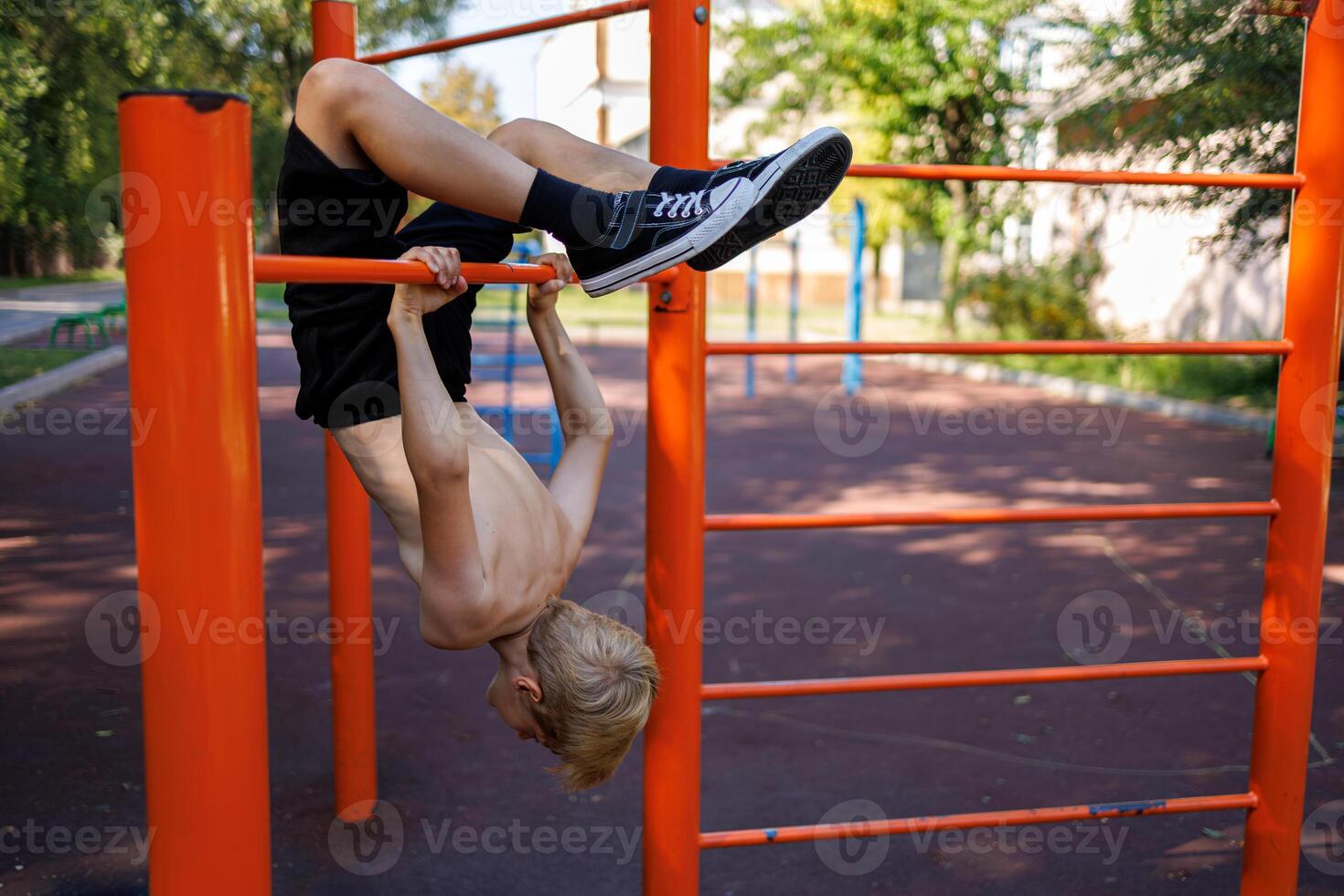 The athletic teenager made a backbend, hanging on the horizontal bar. Street workout on a horizontal bar in the school park. photo