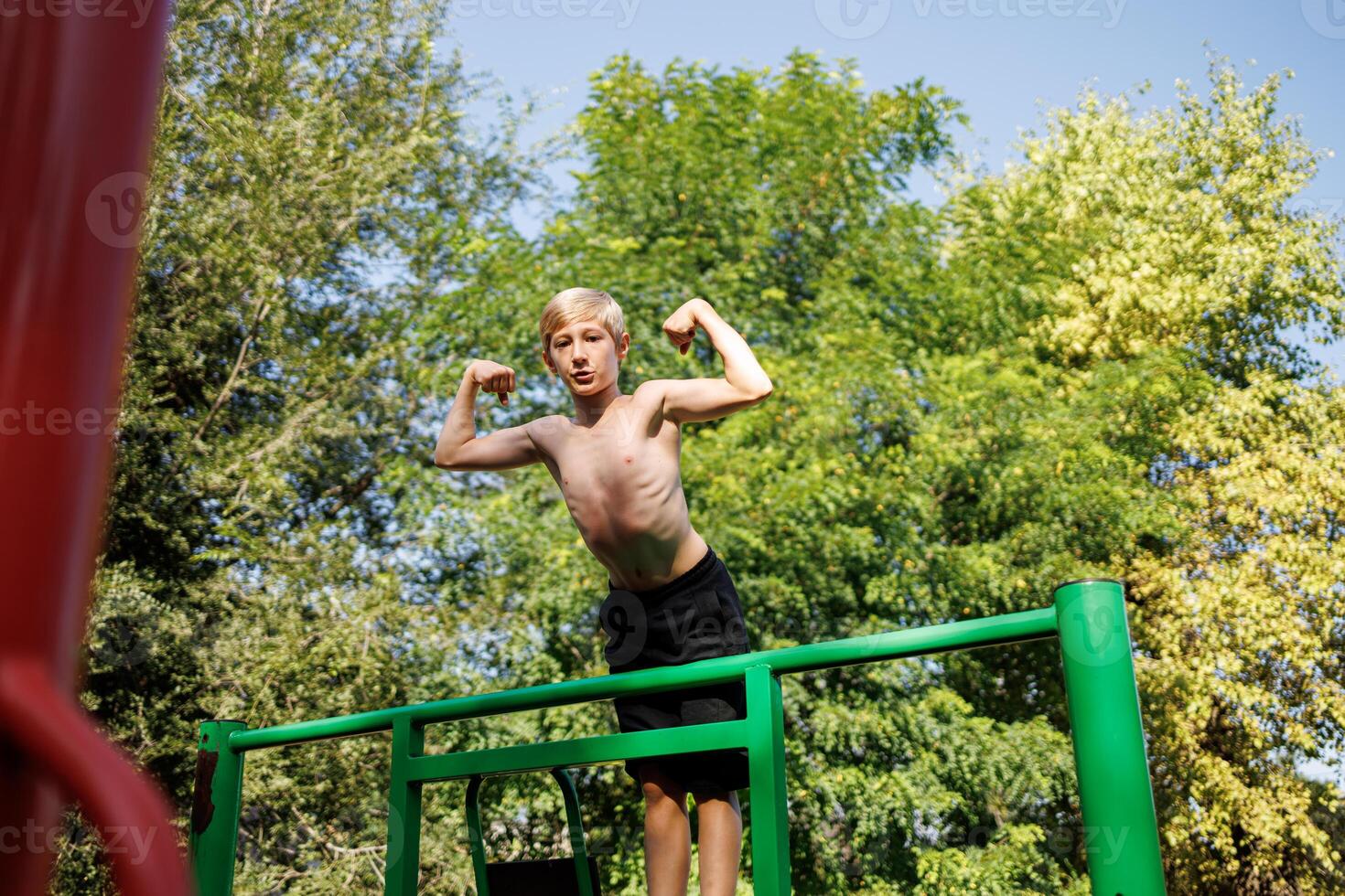 un Deportes niño subido sobre el Deportes horizontal barras y muestra el músculos de el brazos. calle rutina de ejercicio en un horizontal bar en el colegio parque. foto