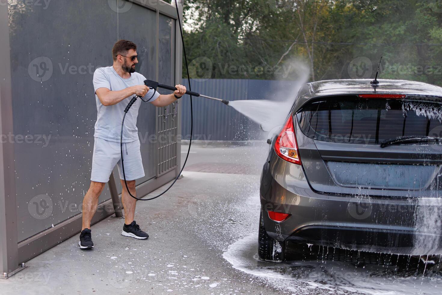 The man has a water cannon in his hand that she uses to wash the car.A car at a self service car wash. photo