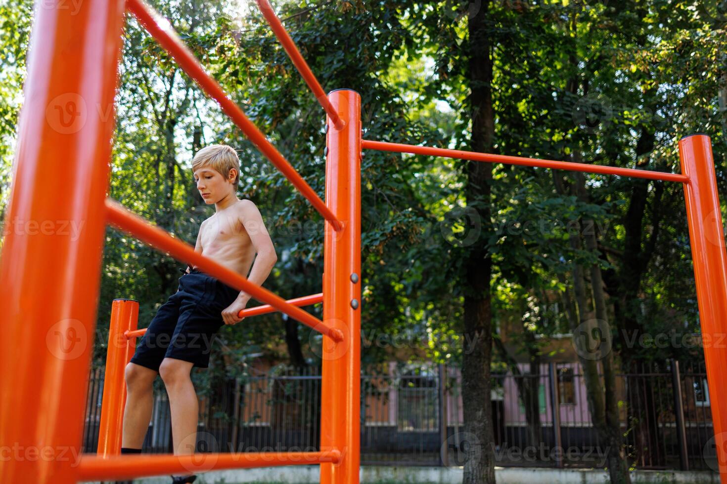 A child athlete sits on the bars of a sports field. Street workout on a horizontal bar in the school park. photo