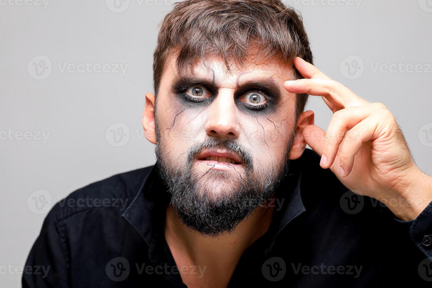 portrait of a bearded man with undead-style makeup who holds his hand near his head photo