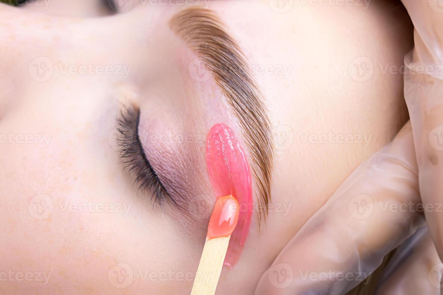 close-up of applying red wax to remove unwanted hairs from the lower contour of the model's eyebrows photo