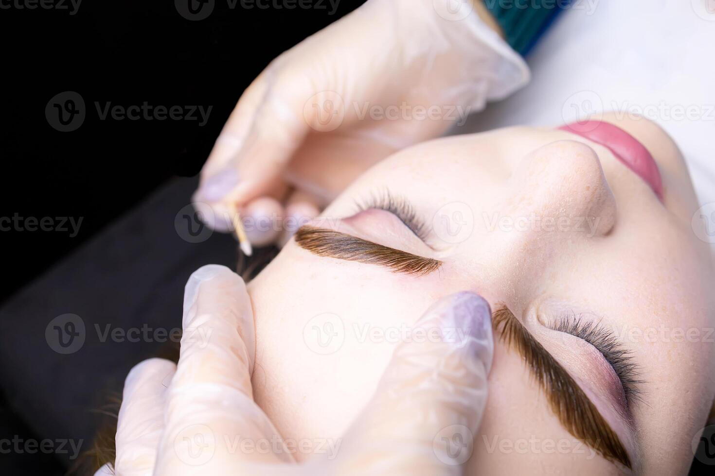 macro photography of the model's eyebrows painted and applied eyebrow paint on them, the master tries to remove excess paint from the contour of the eyebrows with a cotton swab photo