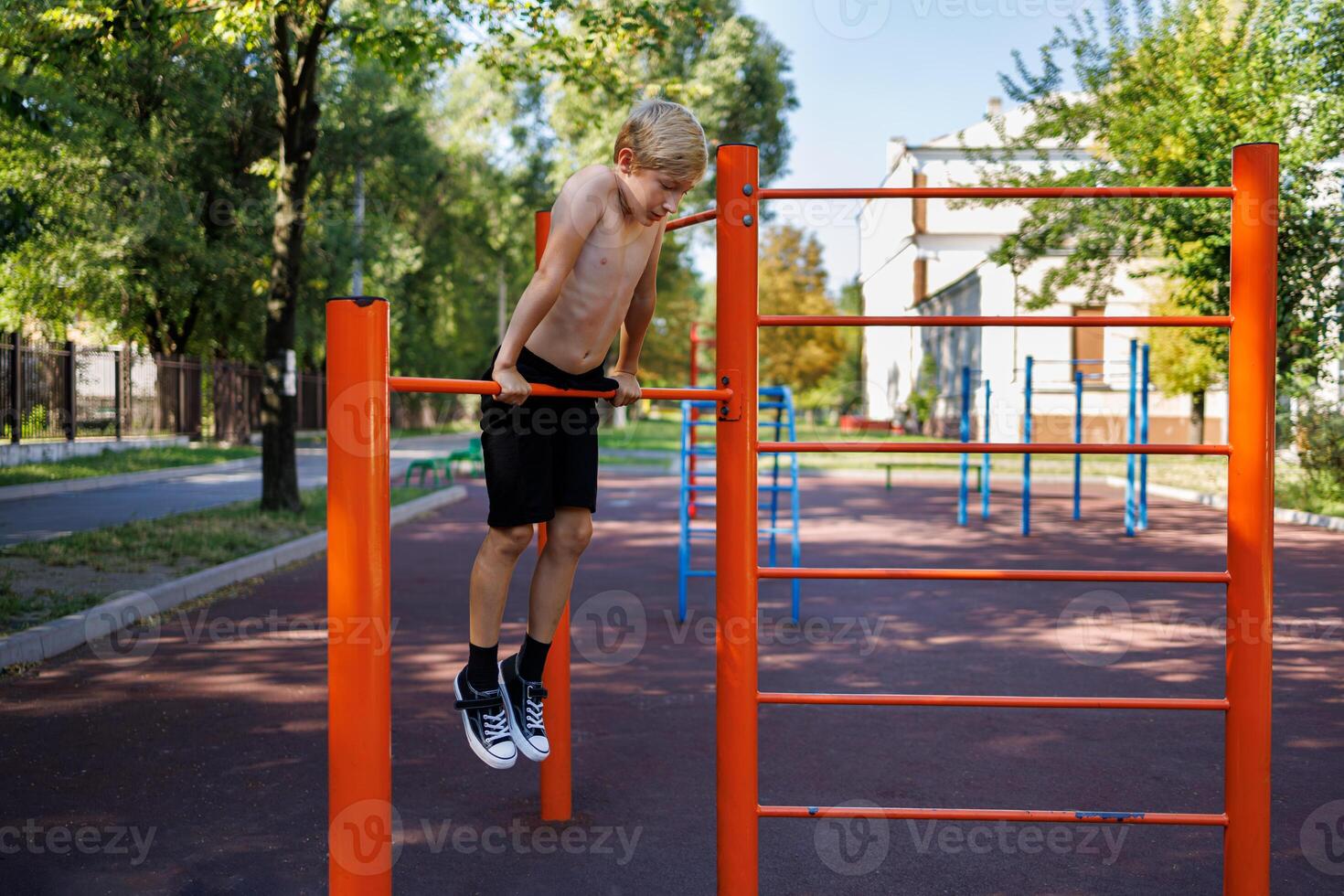 A teenage athlete holds onto the bar with his hands and hangs from it. Street workout on a horizontal bar in the school park. photo