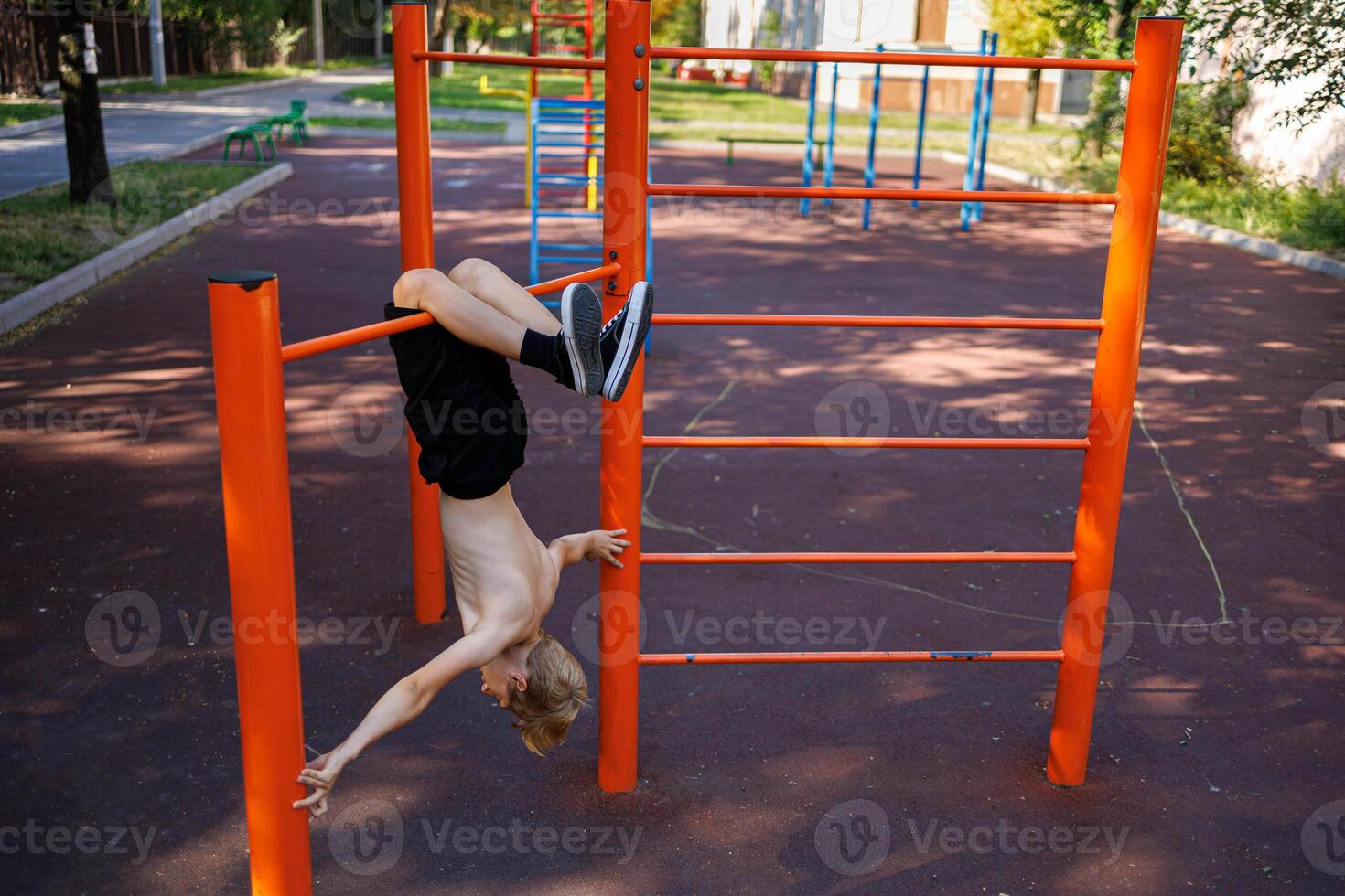 A teenager of athletic build hangs upside down with his feet on the bar. Street workout on a horizontal bar in the school park. photo