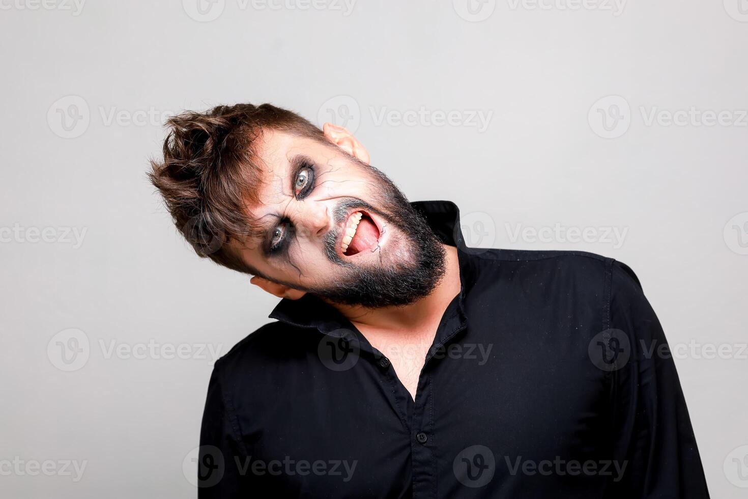 a man with undead-style makeup tilted his head to the side and looks at the camera from under his brows photo