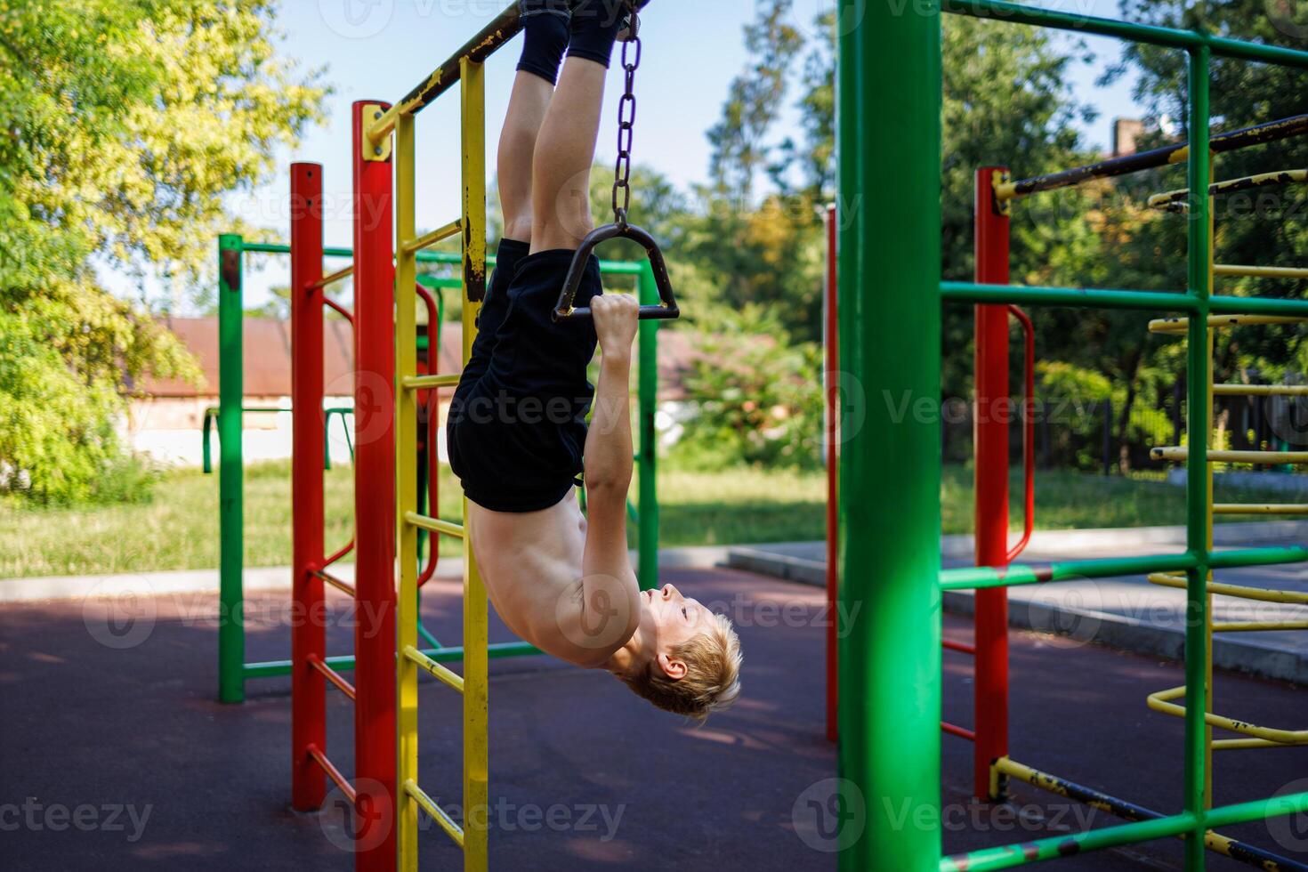 The teenager hangs upside down, holding on to the handles on the chains. Street workout on a horizontal bar in the school park. photo