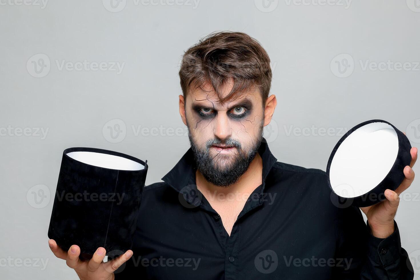 a man with a beard and makeup for Halloween holds a black box with gifts in his hands photo