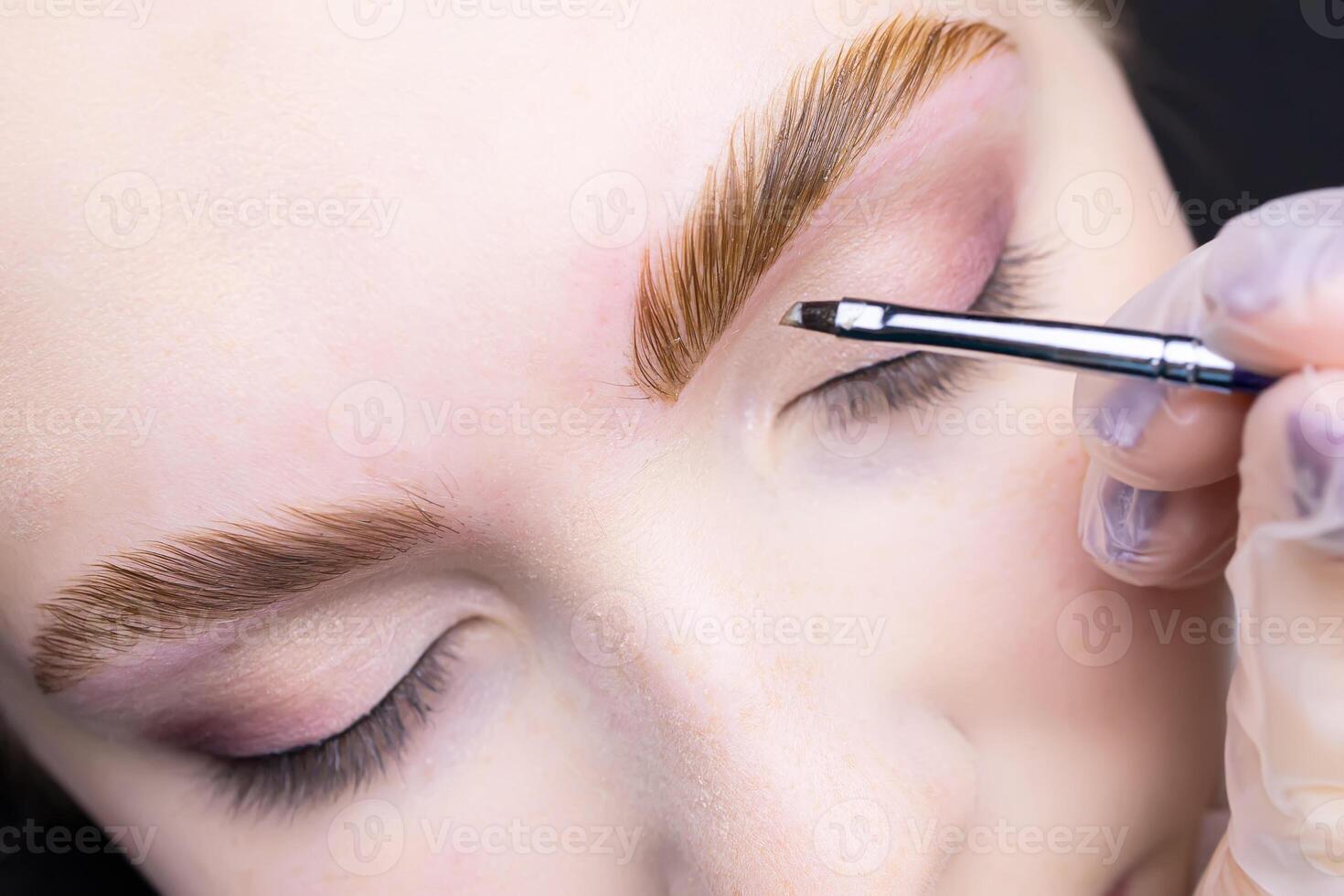 the hands of the master hold a brush and apply paint to the eyebrows of the model coloring the hairs after the lamination procedure photo