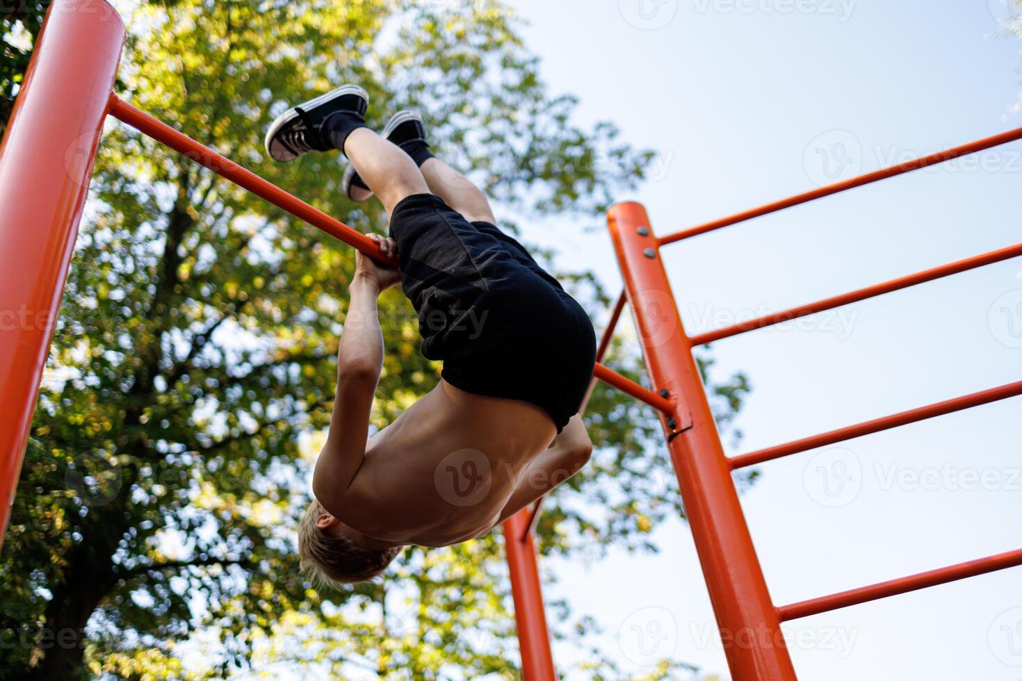 Bottom view of a teenager who performs gymnastic exercises. Street workout on a horizontal bar in the school park. photo