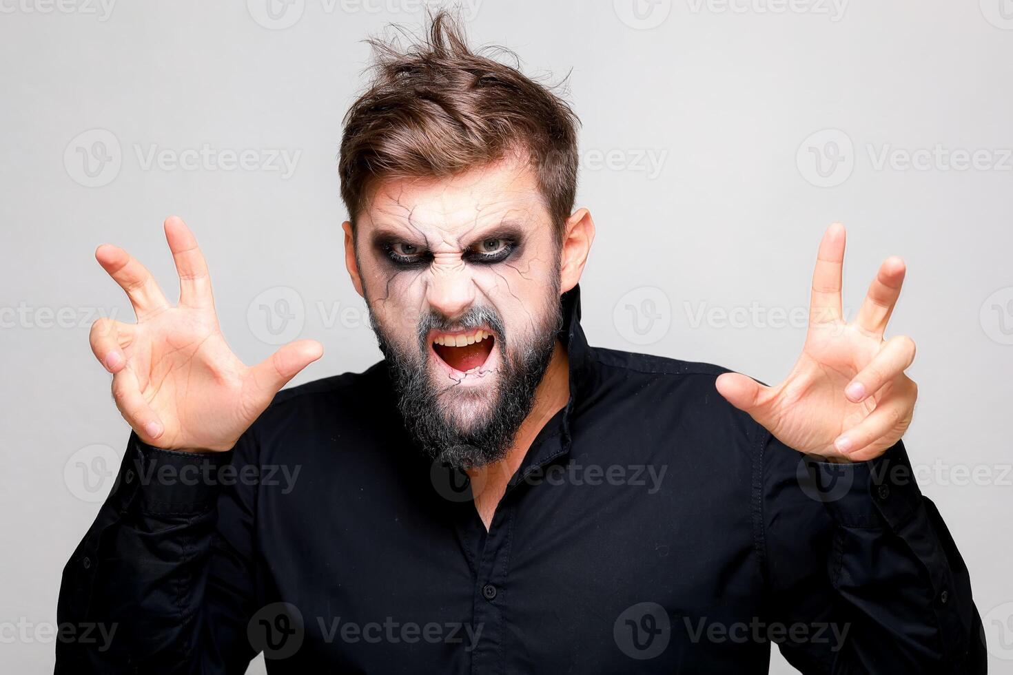 Scary undead-style makeup for Halloween on a bearded man who shows gestures photo