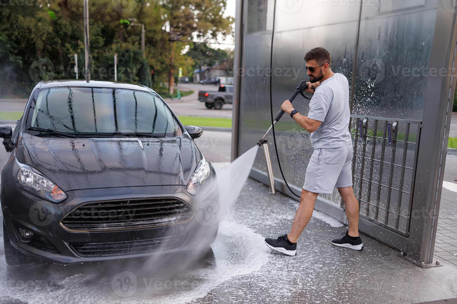 The man aims the water cannon at the car's front headlights and washes them. A car at a self service car wash. photo