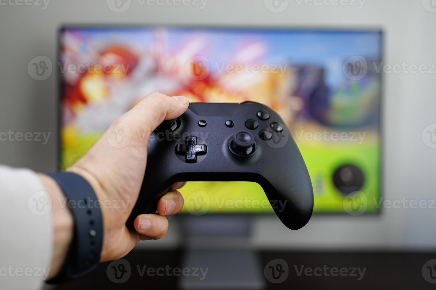 A hand holds a game controller in front of the monitor, game gamepad in hand photo