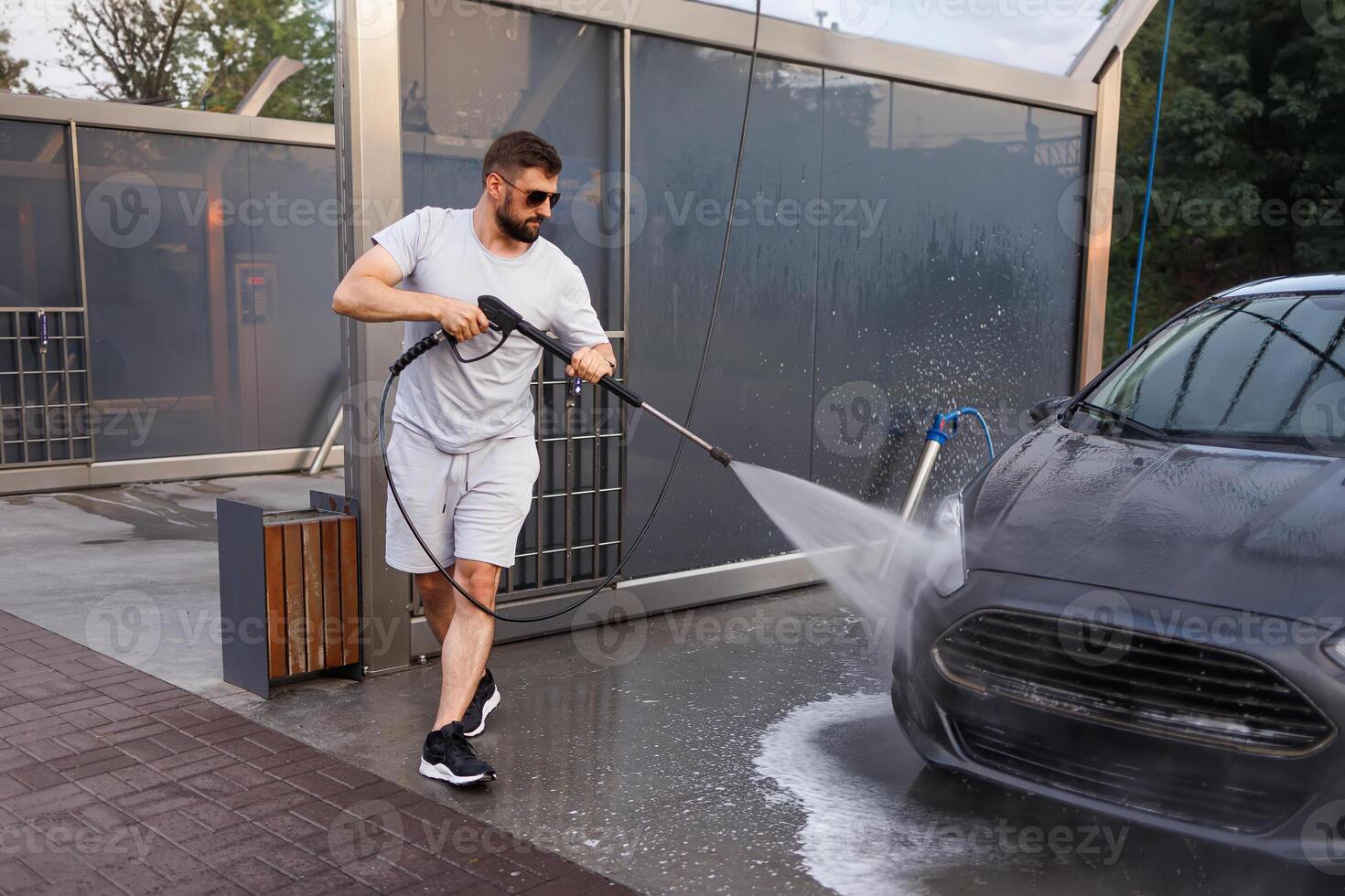 A man washes the front grill of a car with a water cannon. A car at a self service car wash. photo