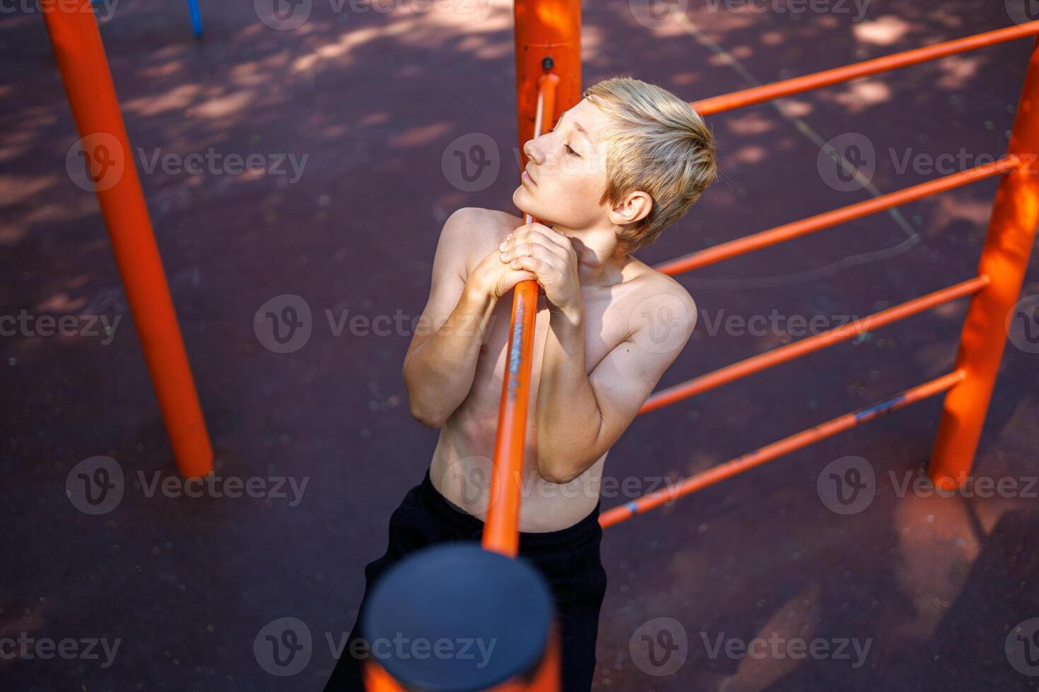 Athletic child performs a lateral pull-up on the bar. Street workout on a horizontal bar in the school park. photo