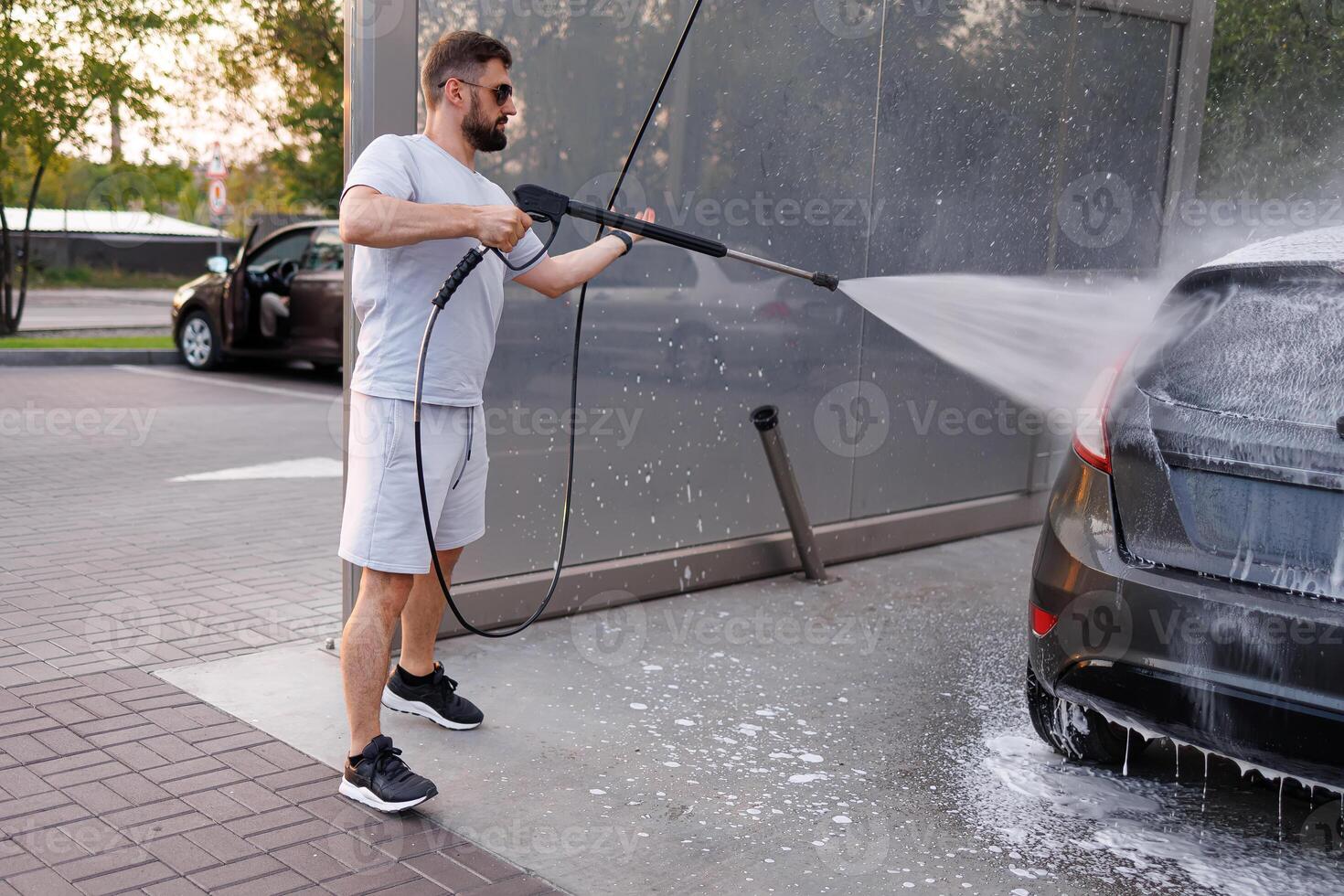 A man washes off foam with a water cannon at a car wash. A car at a self service car wash. photo