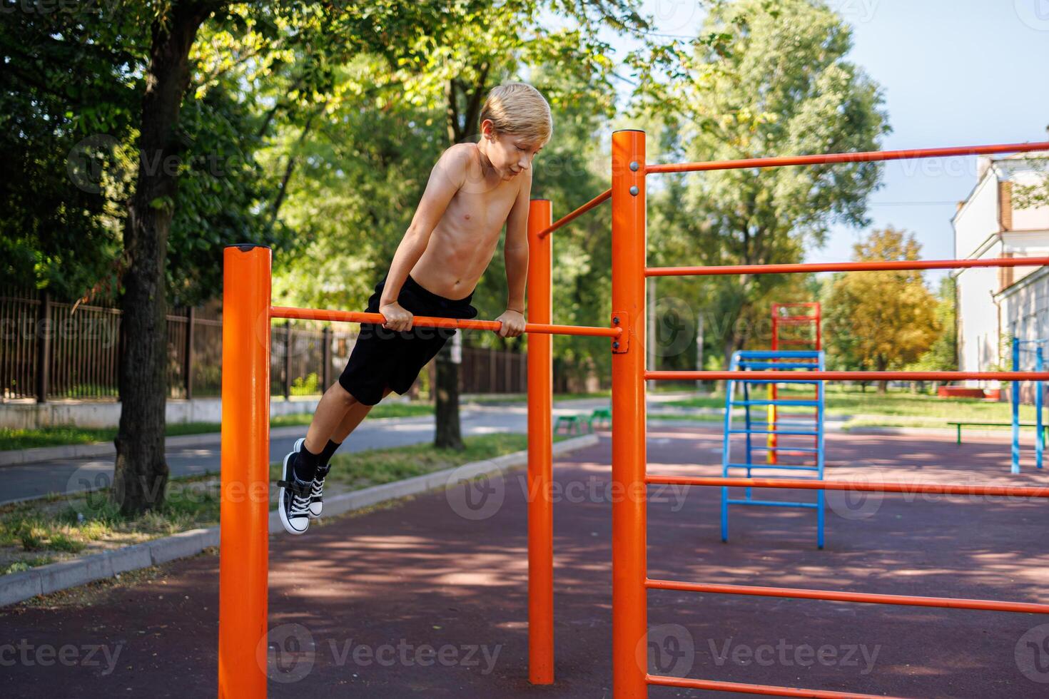 The teenager holds his weight on the extended arms during the execution of the elements on the bars Street workout on a horizontal bar in the school park. photo