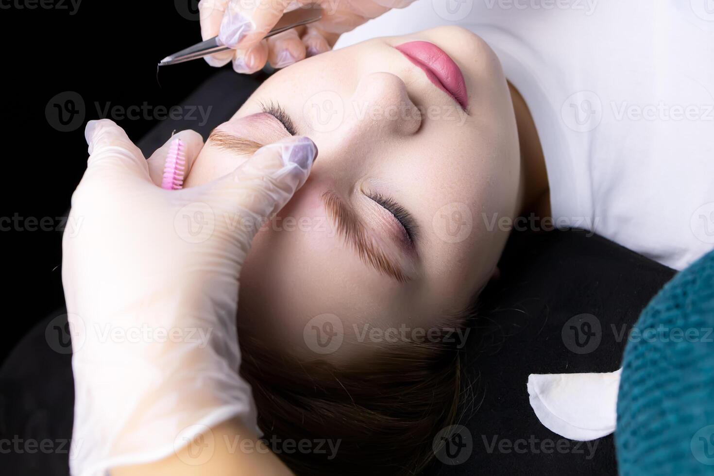 the hands of the master in white gloves perform plucking of excess hairs with tweezers after laminating the eyebrows photo