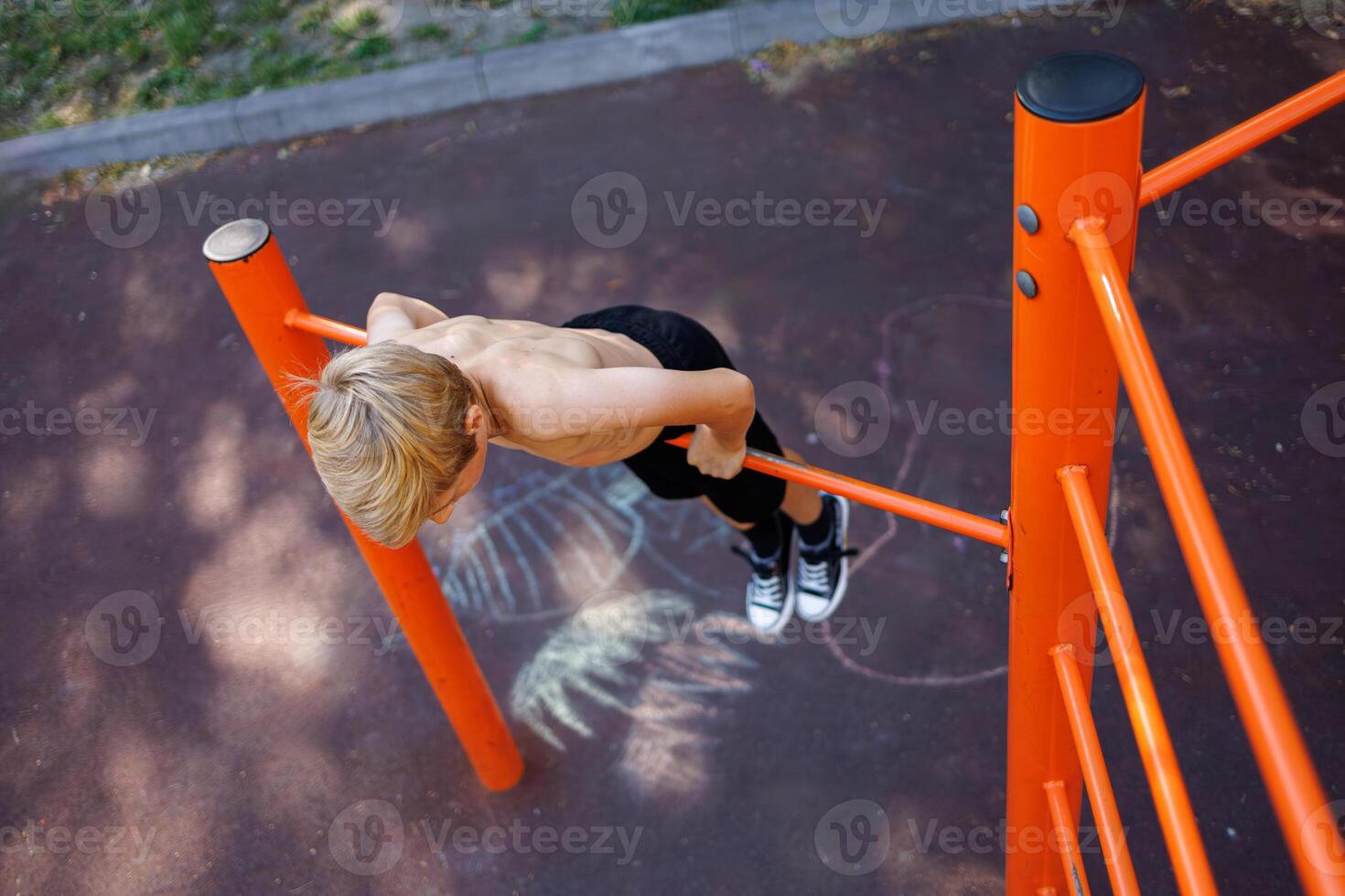 A teenager stretched out holding onto his arms and performing acrobatic exercises on a horizontal bar. Street workout on a horizontal bar in the school park. photo