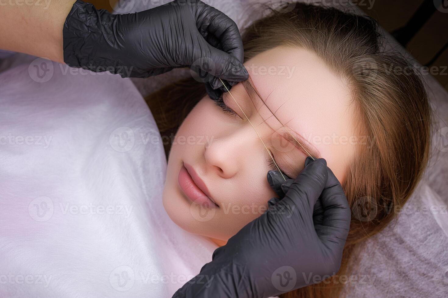 Top view of the model in which the master makes the marking with a thread before the procedure of permanent makeup. PMU Procedure, Permanent Eyebrow Makeup. photo