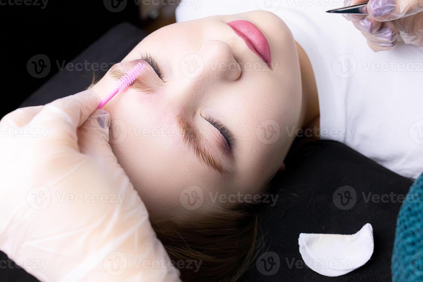 the model's face in close-up combs the model's eyebrows with a pink brush after lamination photo