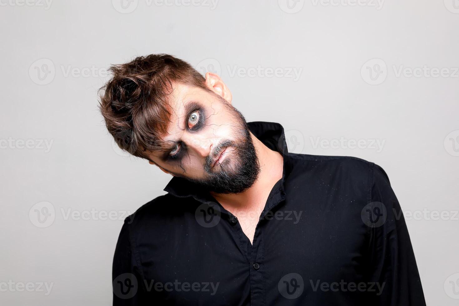 a man with undead-style makeup tilted his head to the side and looks at the camera from under his brows photo