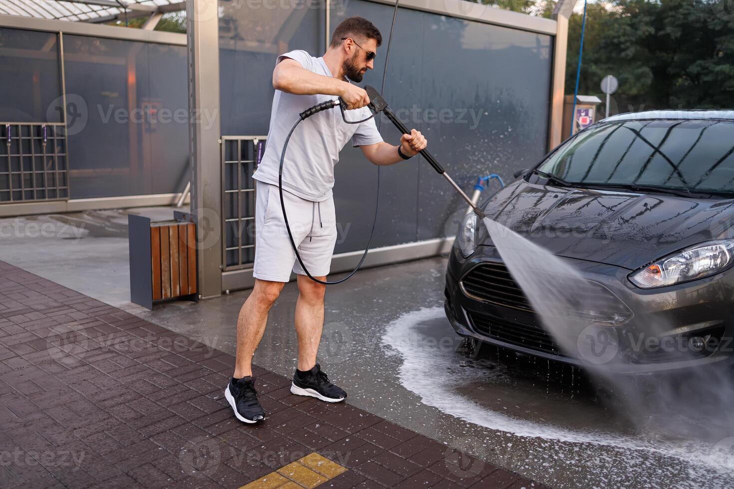 A man washes the front grill of a car with a water cannon. A car at a self service car wash. photo