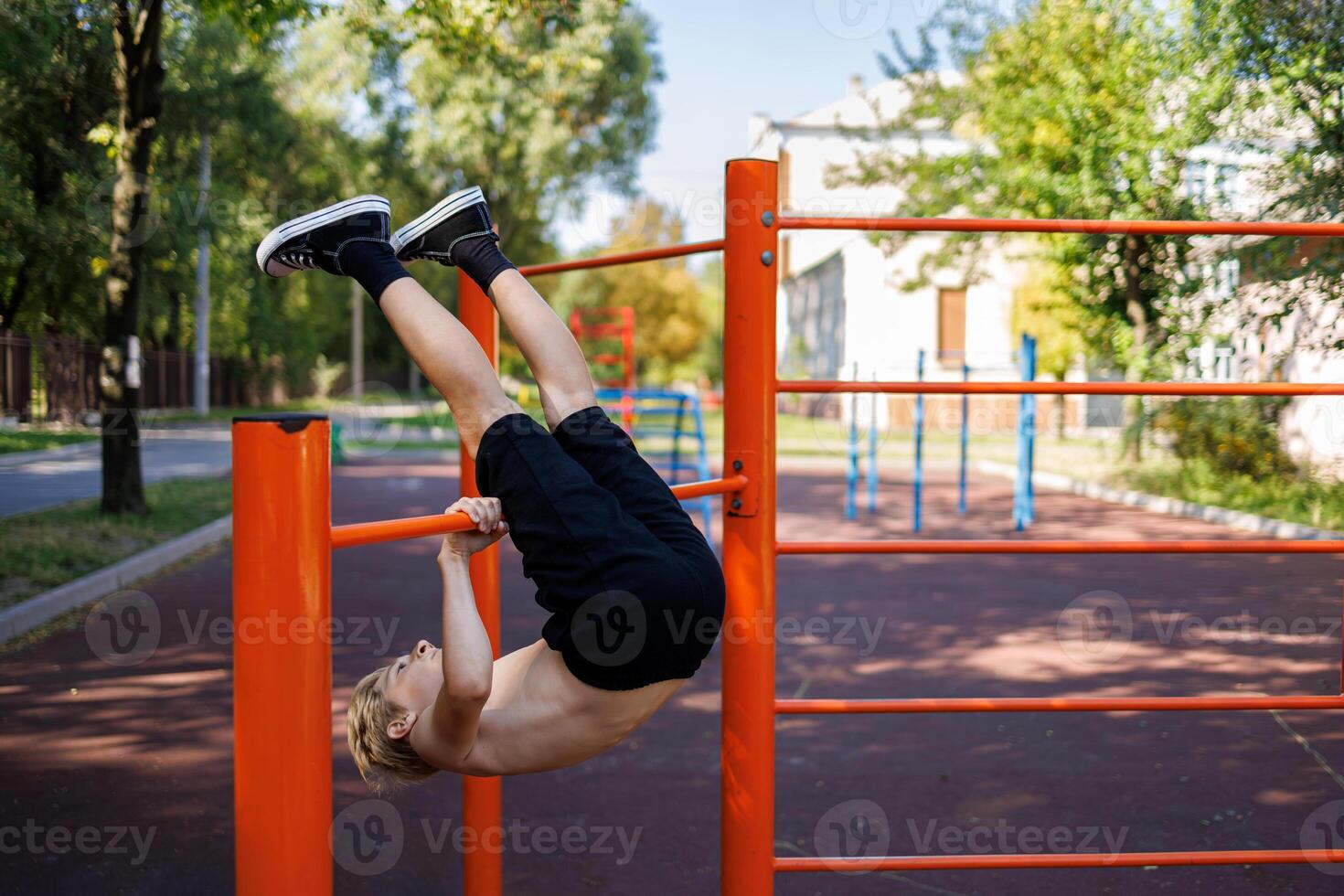 A teenager performs exercises by throwing his legs over the horizontal bar. Street workout on a horizontal bar in the school park. photo